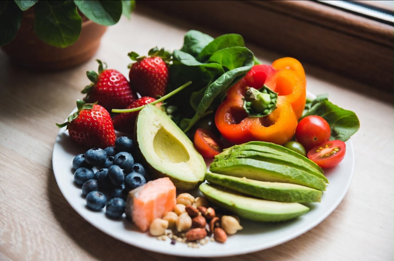 Plate of berries, leafy greens, avocado, salmon, nuts and peppers for skin health